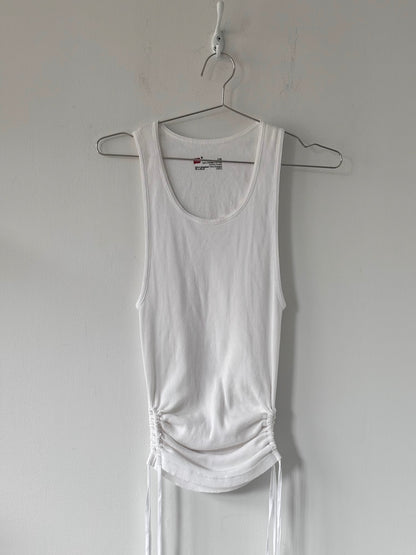 White tank top hanging on a hanger against a plain wall