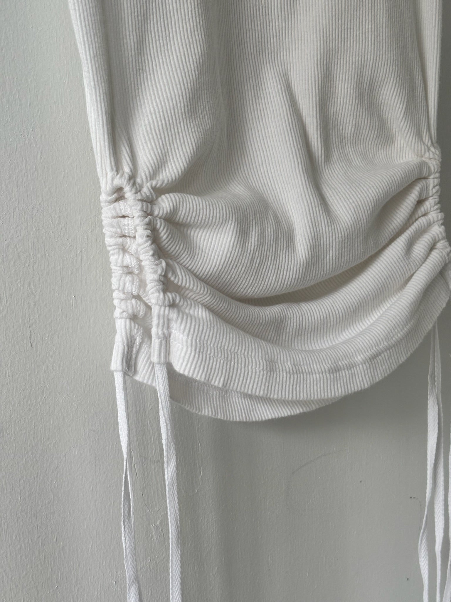 White ribbed knit top with a gathered neckline on a light gray background