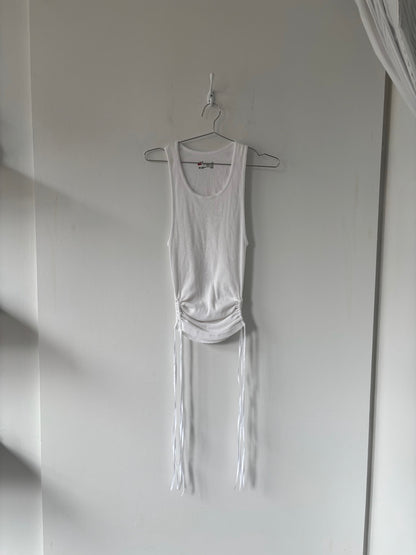 White tank top with fringe details hanging on a hook against a white wall.