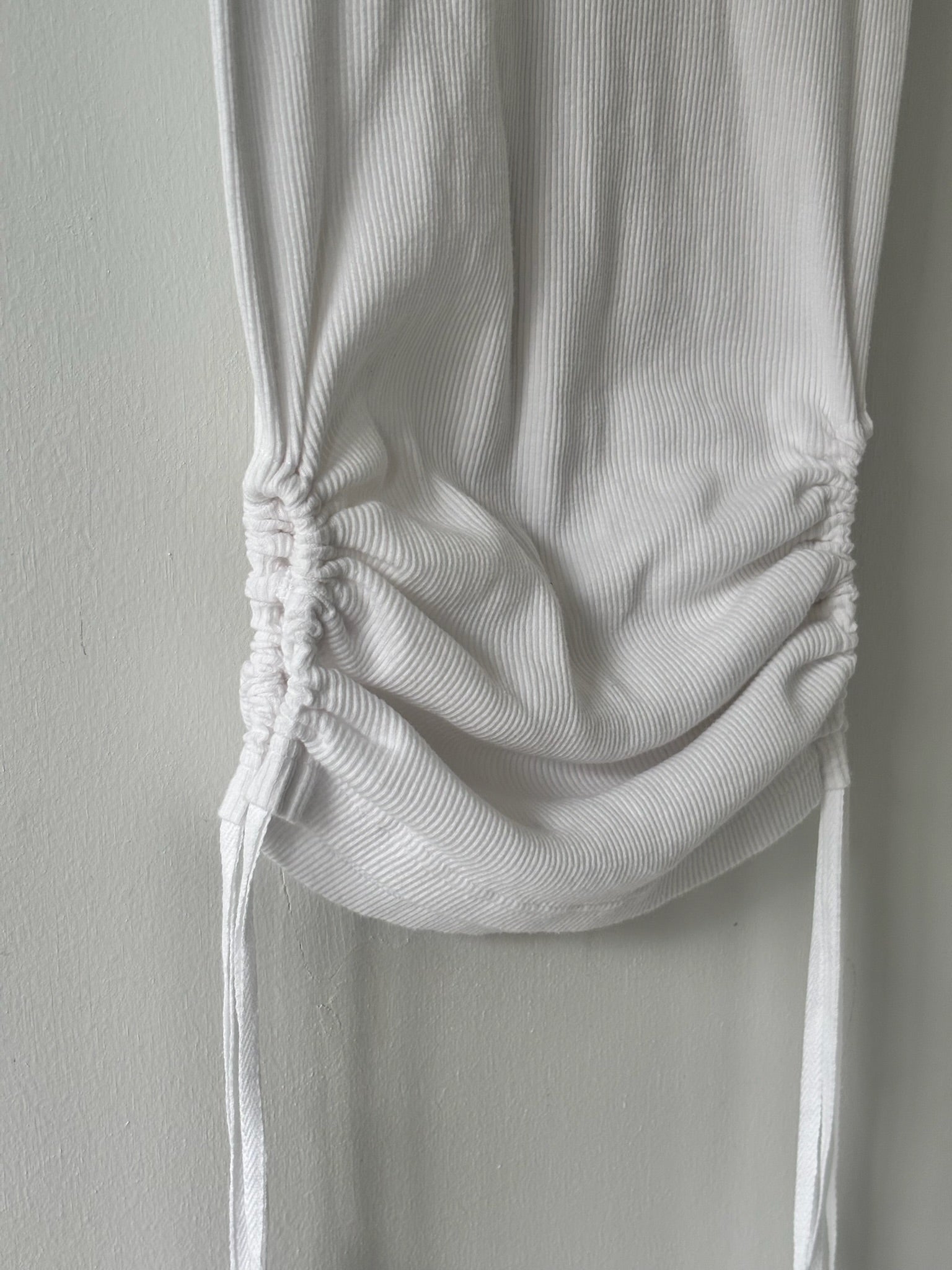 White ribbed tank top with a tie detail on a plain background