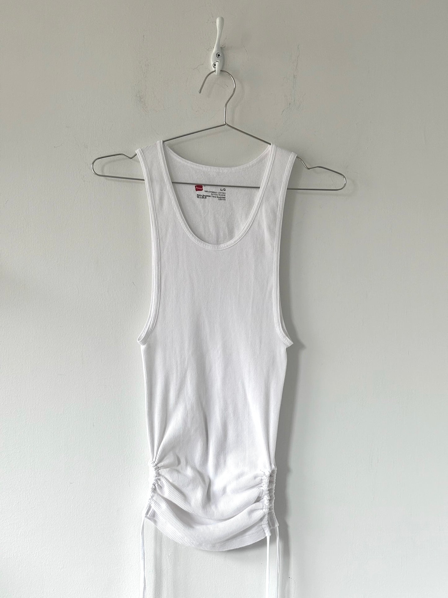 White tank top hanging on a hanger against a plain white background