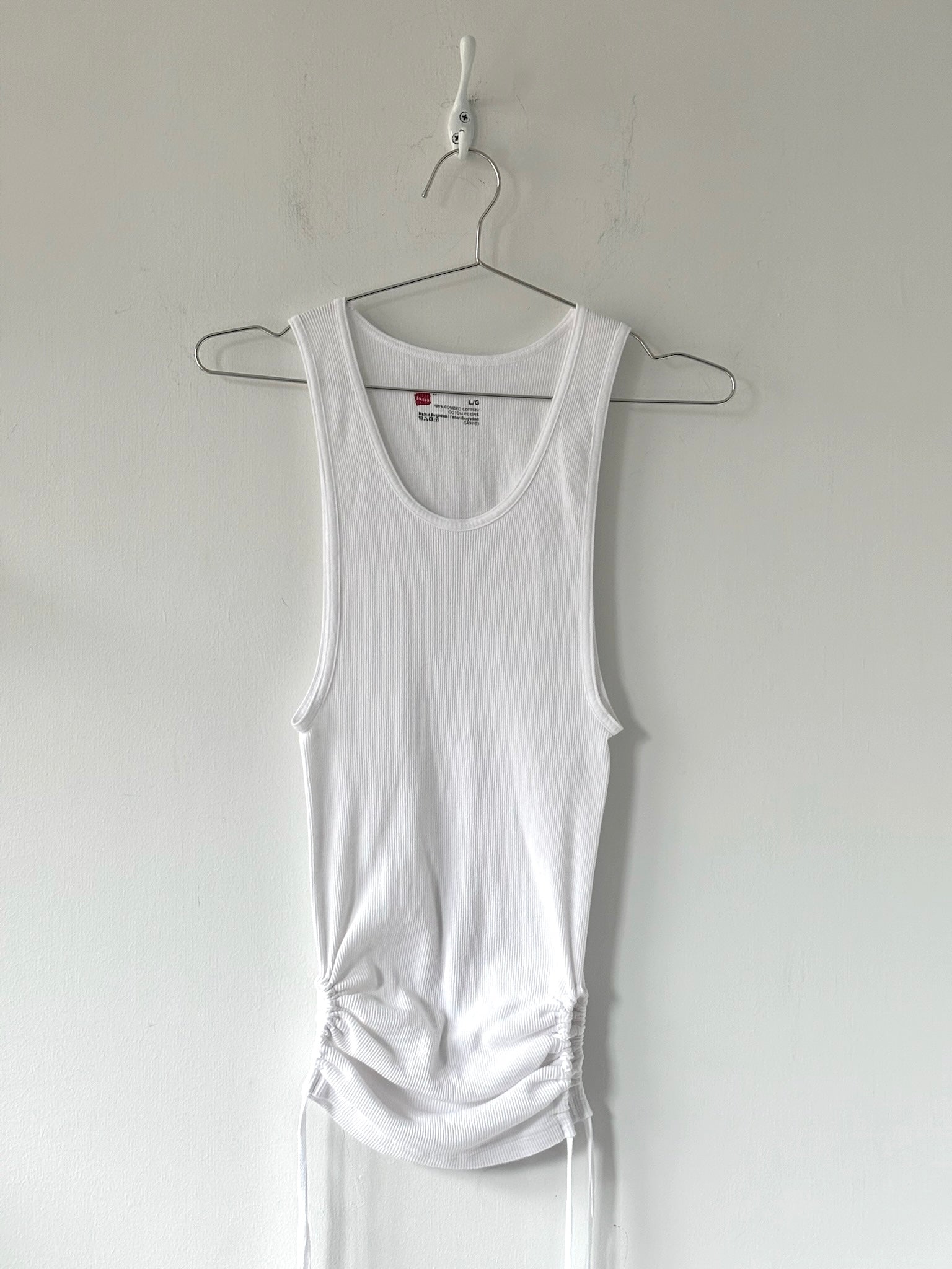 White tank top hanging on a hanger against a plain white background