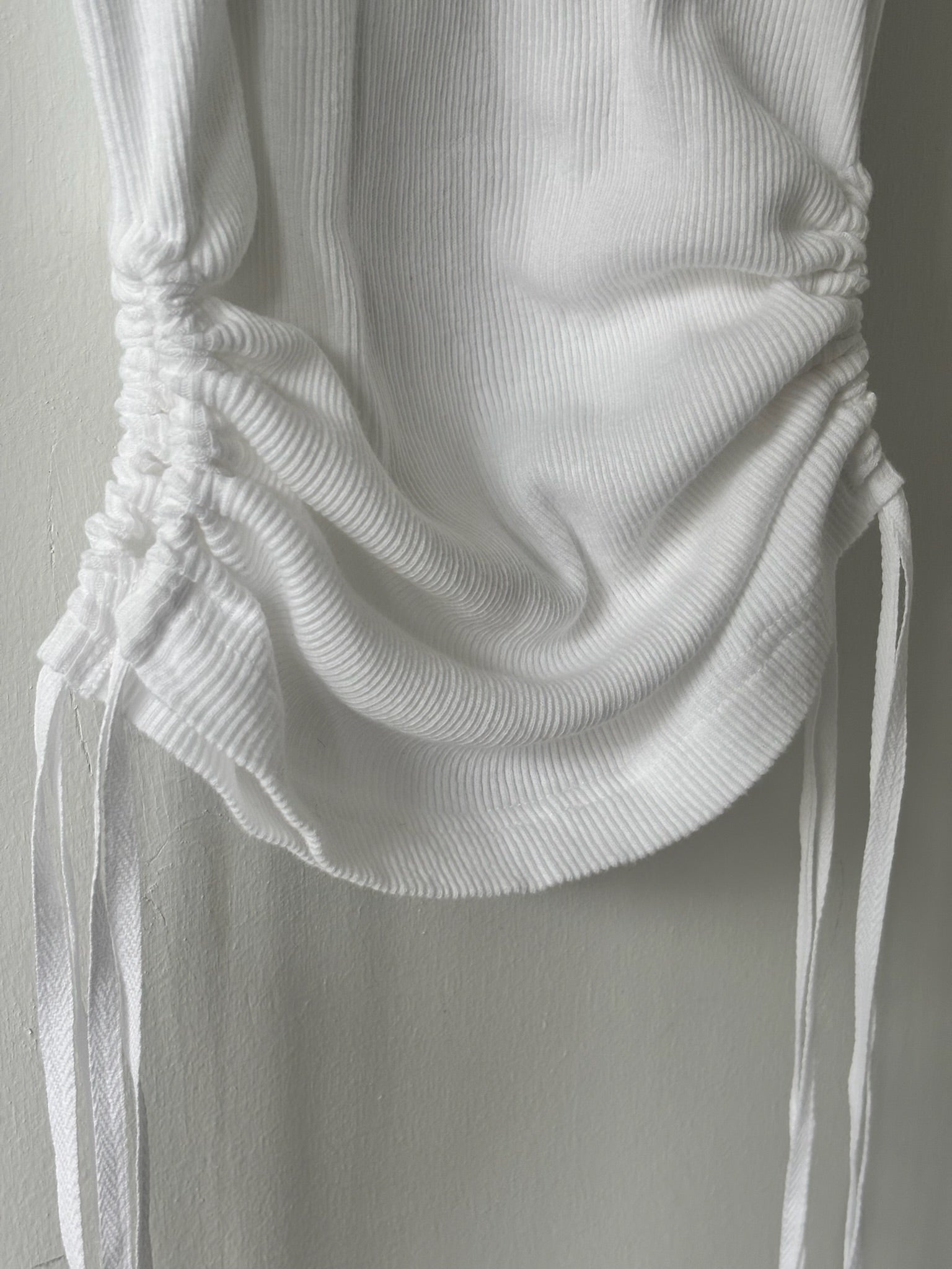 Close-up of a white ribbed knit top with a tied design on a neutral background