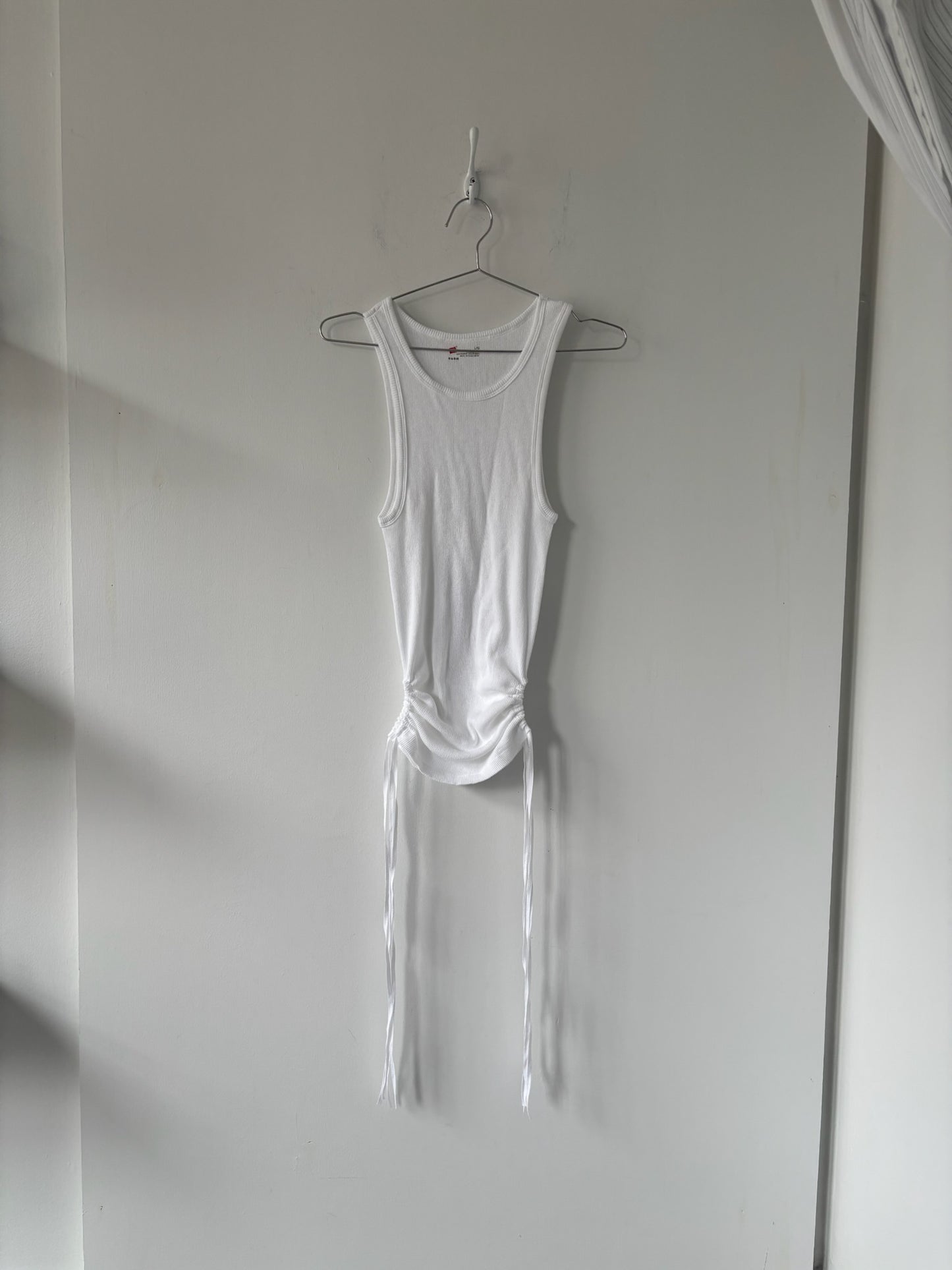 White tank top hanging on a hook against a plain wall
