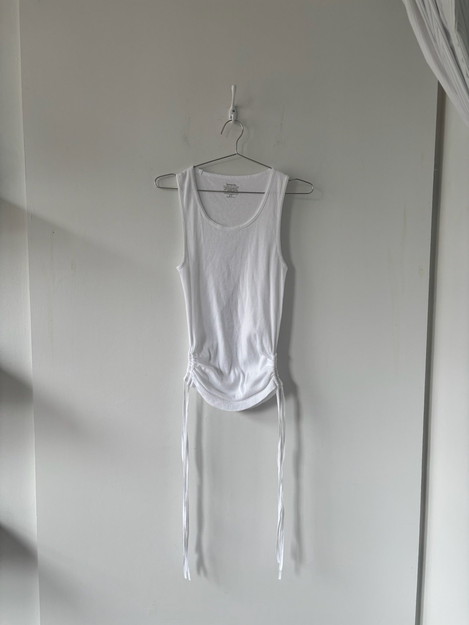 White tank top with ties hanging on a hook against a plain wall.