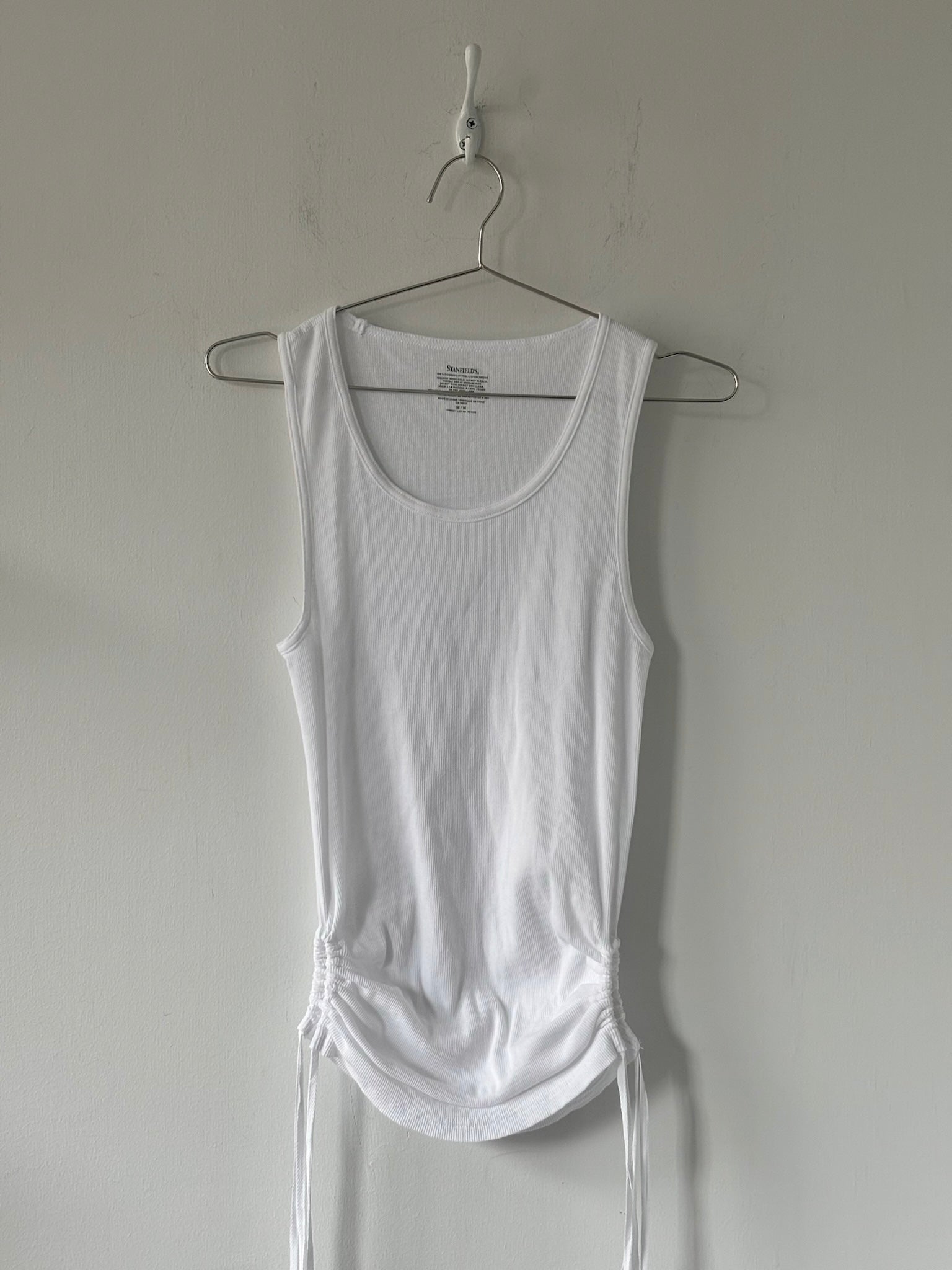 White tank top on a hanger against a plain wall